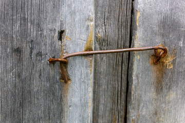 Close-up of weathered, unpainted wooden door, locked on metal hinge. Vintage background from pine shabby plank with rusty lock.