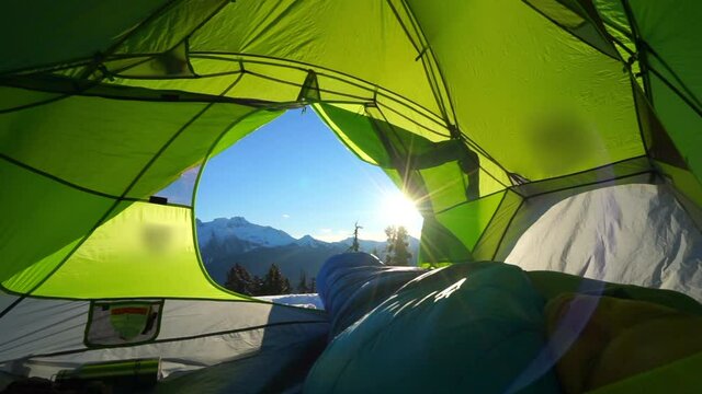 Lockdown shot of man sleeping in green tent snowcapped mountains on sunny day - Elfin Lakes, British Columbia