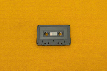 Obraz premium Top View of an old black cassette over a yellow cloth. Fashion and retro music concept