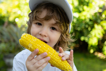 Autumn lifestyle. Homegrown organic food. Vegan children nutrition. Little boy eating corn on the...