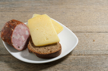 Bread, sausage, cheese on a plate against the background of old village ash planks. Simple breakfast. Selective focus.