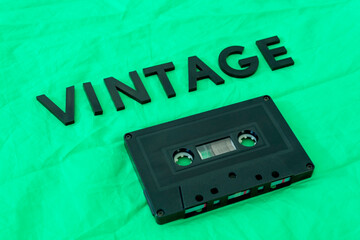 Obraz premium Top View of VINTAGE black lettering word with an old black cassette over a green cloth. Fashion and music concept