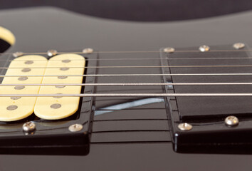 closeup to a six black electric guitar strings, wooden fretboard and microphones . Instruments and music concept