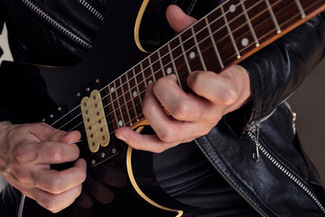 Fototapeta na wymiar Closeup to a man wearing a leather jacket playing a black and yellow electric guitar with black background. Rock and music concept