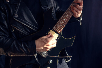 A man wearing a leather jacket playing a black and yellow electric guitar with black background. Rock and music concept