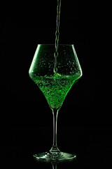 Green drink is poured into a glass. Black background.