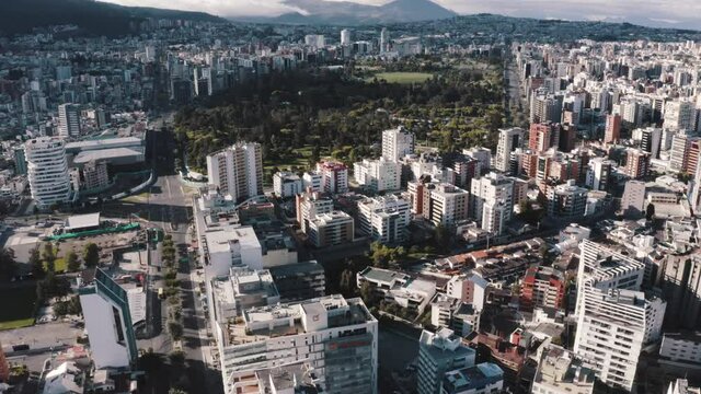 Drone shot of the North part of the city of Quito, Ecuador. Overlooking buildings and in the back, Parque La Carolina during quarantine. Also, mountains and empty streets with trees and houses.