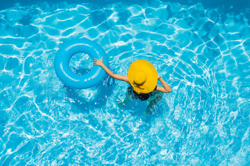 Woman sitting in a swimming pool on a ring pool float in a large yellow sunhat