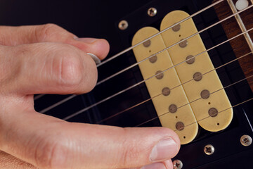 Closeup to a male hand holding a pguitar pick playing a black and yellow electric guitar. Rock &...