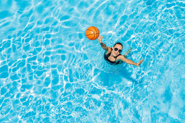 Young woman plays in the pool with a beach ball