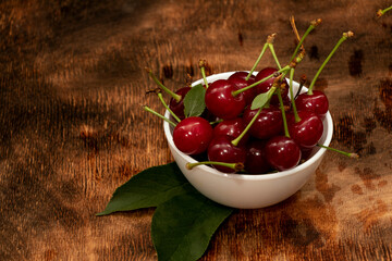 Red berries of a cherry in a white ceramic bowl. On a wooden background. A lot of berries. Summer.