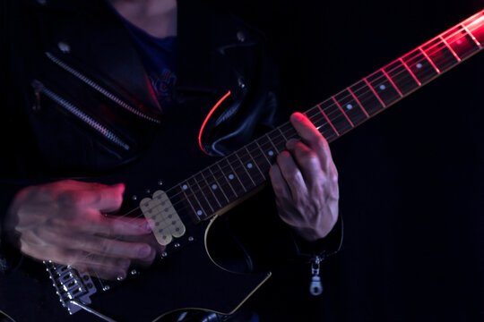 Long Exposure picture of a man wearing a leather jacket playing a black and yellow electric guitar at indoor iluminated with red and white lights. Rock and music concept
