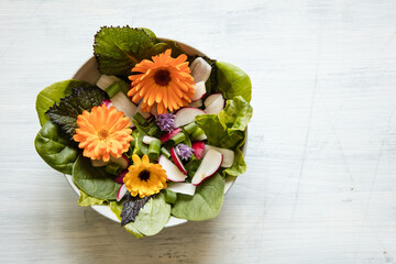 Schale mit Salat und essbaren Blüten auf hellem Holzuntergrund - 357754545