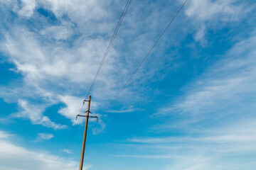  Power line post with electricity cables against a clear sky with white clouds.