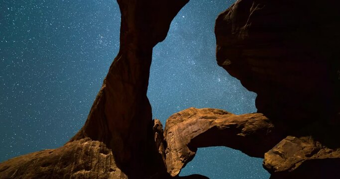 Tilt up time lapse shot of Double Arch in desert against constellation at night - Arches National Park, Utah