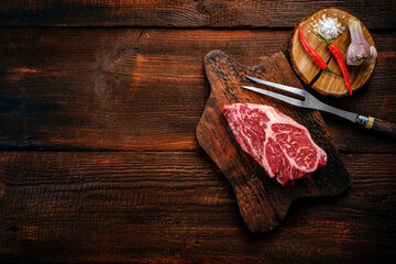 Beef shoulder steak on a wooden table with garlic and red pepper, top view and copy space