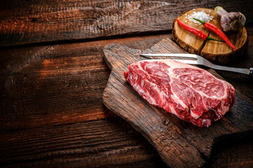 Raw Steak Chuck roll of beef on a wooden table with garlic and red pepper, close up