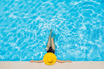 Woman sitting in a swimming pool in a large yellow sunhat - Powered by Adobe