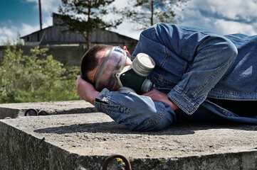 A man in a gas mask lies among the ruins and the dramatic sky background. Biohazard concept....