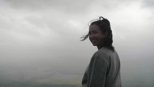 Woman turns, looks at camera and smiles on grey, windy and gloomy day