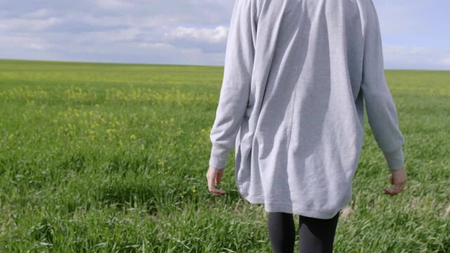 Young woman walking aimlessly in green summer field with wildflowers