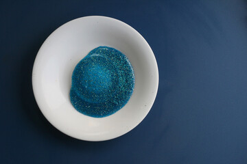 White saucer with shiny blue liquid on a blue background