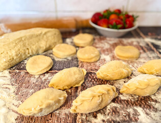 Uncooked dumplings with strawberries and dough on an abstract wooden surface. The process of preparing a traditional meal of flour dough.