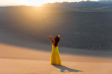 Woman walking alone silhouette in the desert sandy dunes landscape on sunset sunrise and looking at...