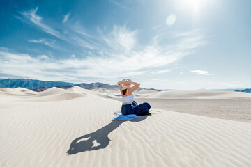 Woman walking alone in the desert dunes landscape and looking at horizon line. Girl dressed in blue skirt, white top, white scarf and hat sitting in Dumont dunes, California in Mojave Desert.