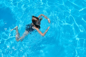 Fototapeta premium Kid has fun in an outdoor pool, child girl swims, dives, plays on the water, blue background