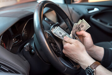 Man  sitting in a car counting dollar banknotes for or as bribes, insurance or credit, investing