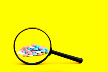 A look through a magnifying glass at a pile of multicolored pills on a yellow background. Search...