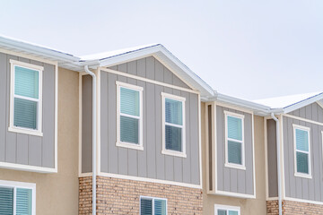 Snowy roof brick wall and vertical siding at exterior of townhome against sky