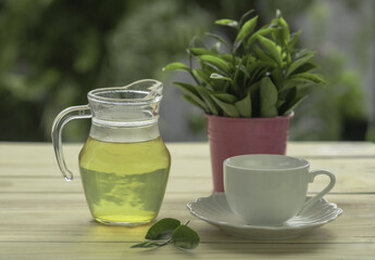 Hot tea in glass jar with cup of tea and tea leaves in pink tin on wooden board