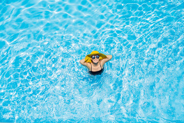 Woman sitting in a swimming pool in a large yellow sunhat