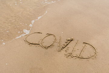 Covid written on the sand of a beach with wave washing, erasing or canceling it during Coronavirus summer, Covid free, STOP Covid, safe beach