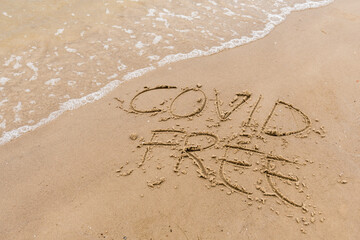 Covid written on the sand of a beach with wave washing, erasing or canceling it during Coronavirus summer, Covid free, STOP Covid, safe beach
