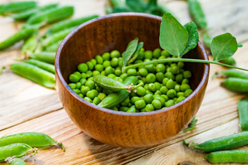 closeup green peas in brown dish, on wooden table.