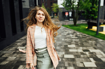 Beautiful girl walks in the city near the black wall in the rain