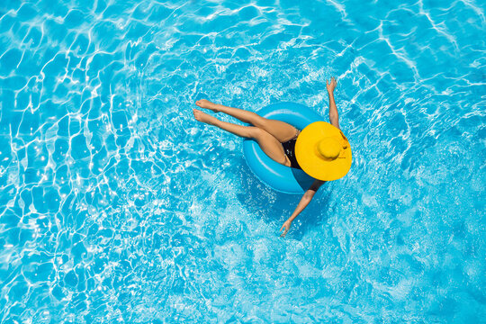 Woman sitting in a swimming pool on a ring pool float in a large yellow sunhat