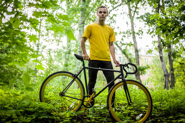 Naklejka premium A young Man stopped to rest With his Bicycle in a public Park. He enjoys an early Sunny morning in the forest.