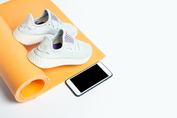 Fototapeta na wymiar Yoga mat, sneakers and phone on a white background. Sports, yoga and training. Top view, flat lay