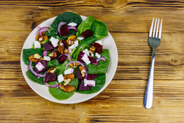 Tasty spinach salad with boiled beetroot, feta cheese, walnut and red onion on wooden table. Top view. Healthy vegetarian food