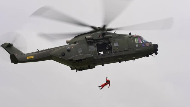 Rescue helicopter crew rescuing ground  crew via wire lifting