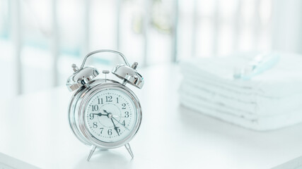 Alarm clock with soft light bathroom decor for advertising, design, cover, green small flowers in vase, towels on white wooden shelf. mock up, copy space