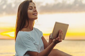 Young woman in straw hat working on a tablet on a beach.  Working on a vacation concept.