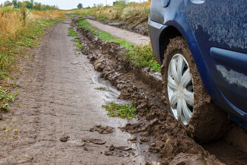A muddy unpaved rural road and a car wheel in the mud