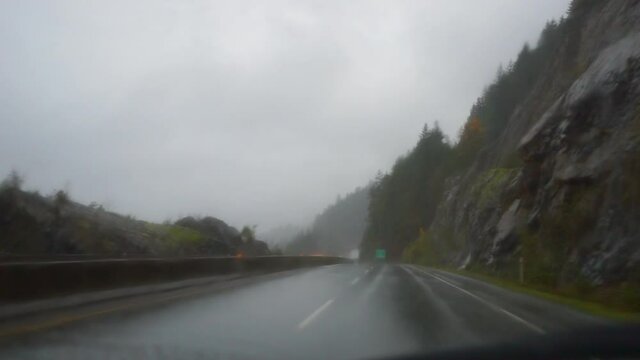 POV shot of vehicles on wet winding road by rock formation on mountain during rainy season - Elfin Lakes, British Columbia