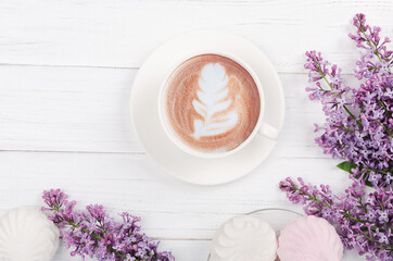 Lilac, coffee with latte art on light wooden table. Romantic morning.Flat lay