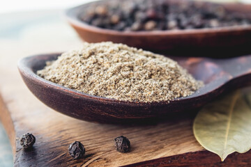Ground black pepper in a spoon lies on a cutting board near the bay leaf and black pepper on a background of blue boards.